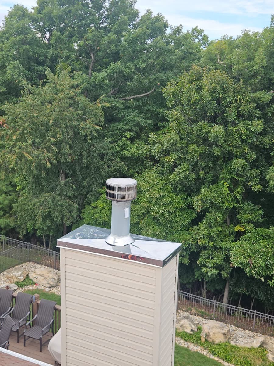 New stainless steel chase cover and chimney cap on top of a vinyl-sided chimney chase, seen from the roof