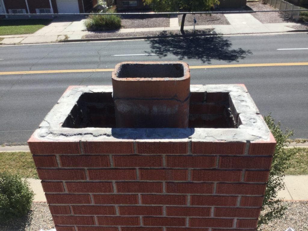 Top of a red brick chimney with a crumbling, patched mortar crown around an uncapped flue tile