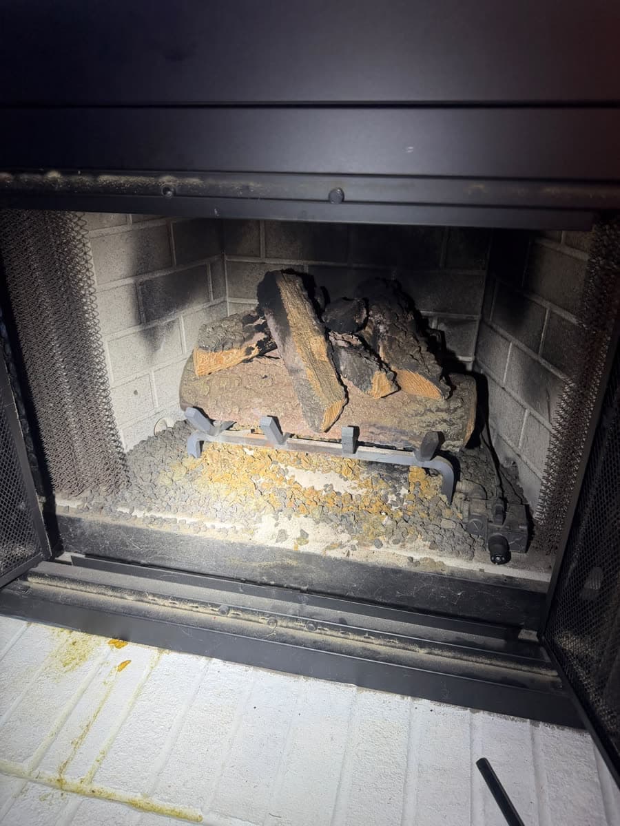 Gas fireplace before service, with ceramic logs out of position and dust and debris covering the burner and ember bed