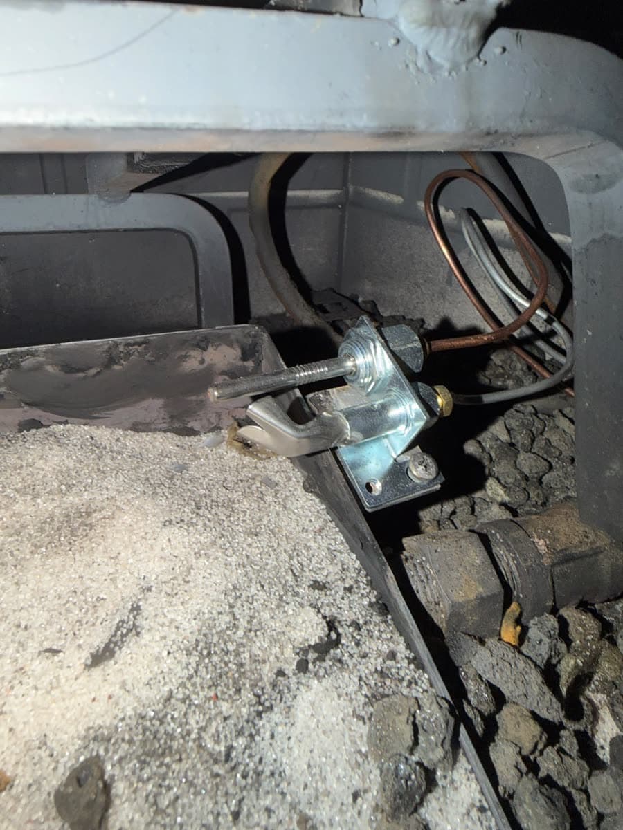 Close-up of a gas fireplace pilot assembly and gas valve beside the burner, exposed for testing during a service